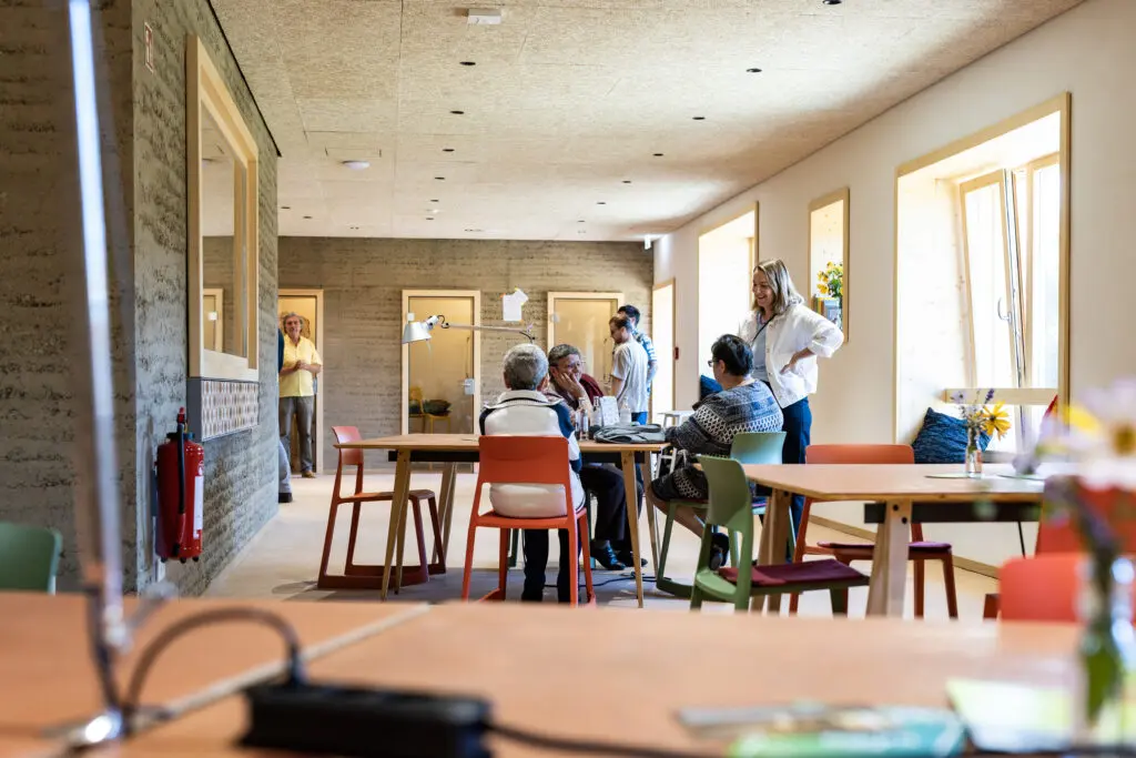 Mehrere Personen arbeiten und diskutieren gemeinsam in einem hellen Coworking-Space mit großen Fenstern und Holztischen.
